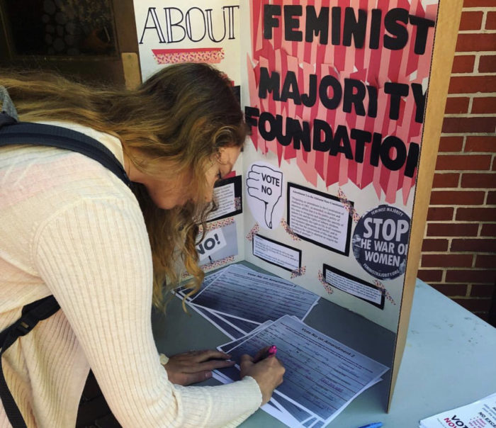A student signs the pledge to Vote No on Amendment 2 at a tabling event.